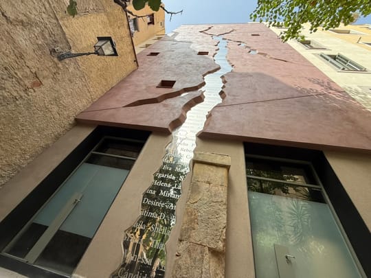 The L'escletxa memorial, a mirrored crack across a building façade at the junction of Carrer de la Pescateria and Carrer d'en Tripó in El Born, Barcelona.