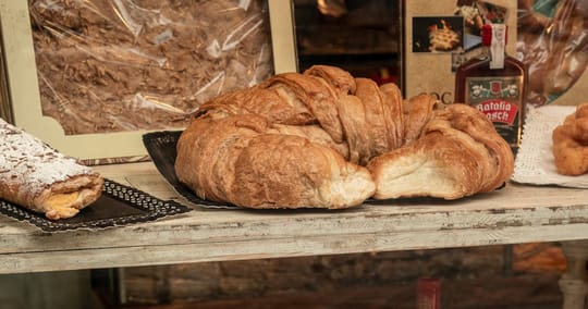 A large laminated pastry on a bakery counter, with a bottle of Catalan ratafia behind it