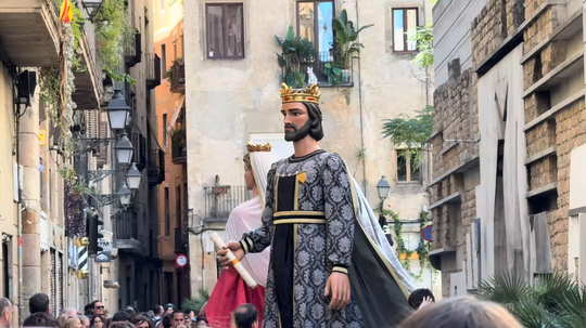 Plaça Nova in Barcelona's Gothic Quarter during the Sant Roc festivities, with crowds gathered around traditional giant figures in front of the Cathedral.