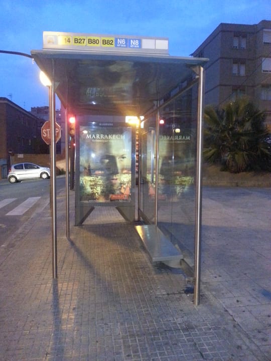 A modern AMB bus on a residential street in Santa Coloma de Gramenet, with passengers boarding under a covered stop.