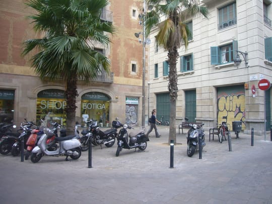 A vintage black-and-white photo of a circus performer on a tightrope above a Barcelona street, with crowds watching below and balconies filled with onlookers in the background.