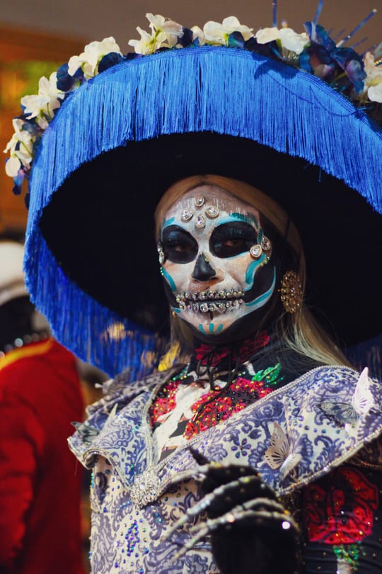 A vibrant procession of elaborately dressed Catrinas walks along the waterfront at Port Vell in Barcelona.