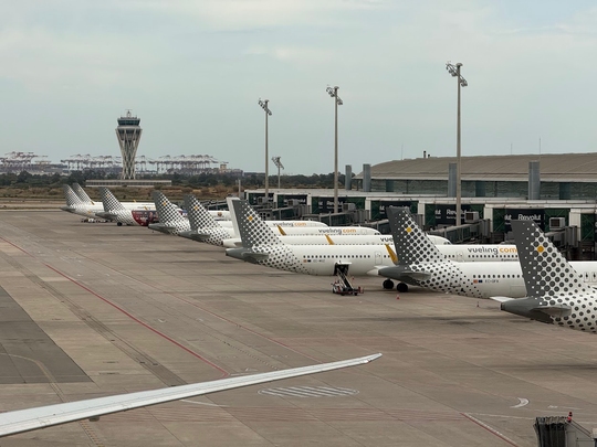 Aerial view of Barcelona-El Prat Airport with aircraft on runways and terminals under a clear autumn sky.