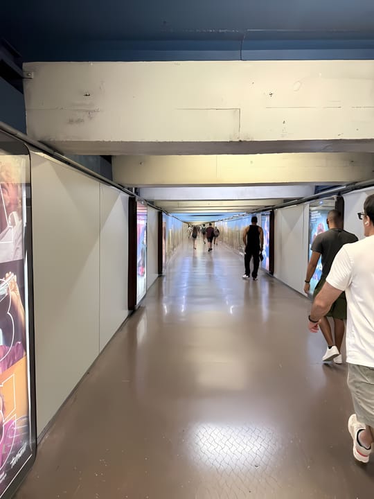 Interior view of the Plaça Catalunya metro interchange hall in Barcelona, showing a tiled corridor with lighting fixtures and signs for lines L1 and L3.