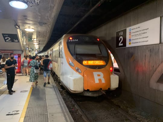 A train from the Rodalies de Catalunya network arriving at Barcelona Sants station, with commuters on the platform.