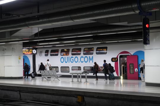 A high-speed Ouigo train at Barcelona Sants station, with digital departure boards showing delays on the Madrid line following a fire in Aragon.