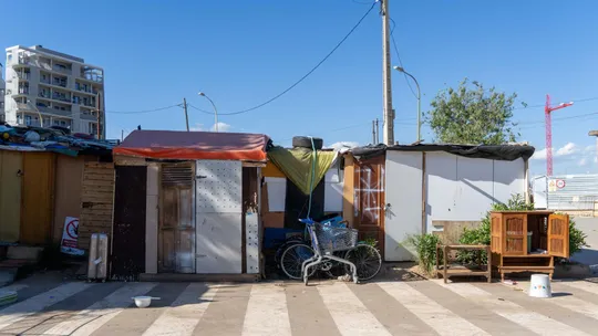 Improvised shacks made of scrap metal and wood, with laundry hanging outside, in a dusty, open field next to railway tracks i