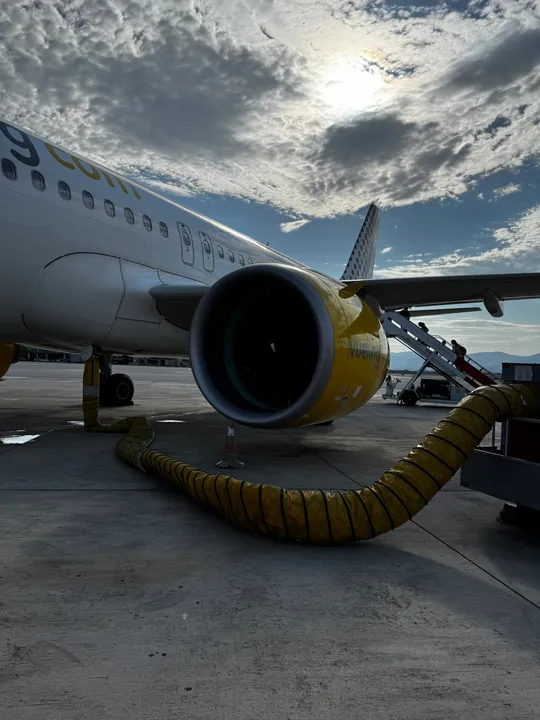 A Vueling plane on the airport tarmac with passengers boarding by mobile steps under a cloudy sky.