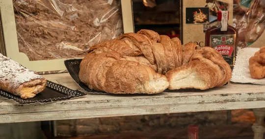 A large laminated pastry on a bakery counter, with a bottle of Catalan ratafia behind it