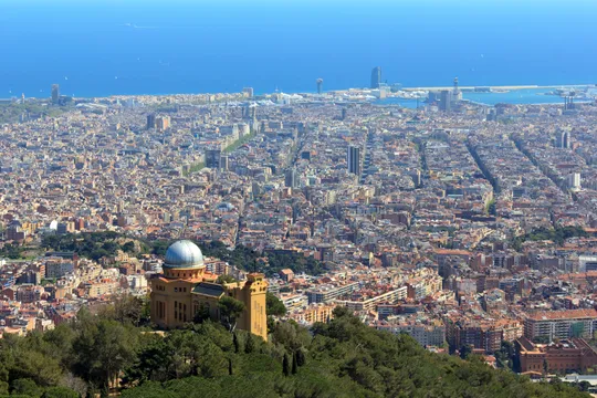 A view of the Fabra Observatory on Montjuïc hill in Barcelona, under a partly cloudy sky, with the city visible below.