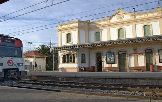 Exterior view of Castelldefels railway station with trains on the platform, located in the Barcelona metropolitan area.