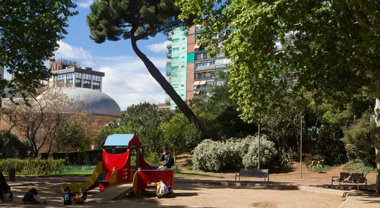 A winding, multi-coloured sensory playground structure called 'Cuc sensorial' set within green gardens in Barcelona's Sarrià neighbourhood.