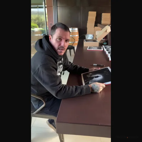 Spanish singer Dani Martin seated at a table, speaking to the camera while signing prints.
