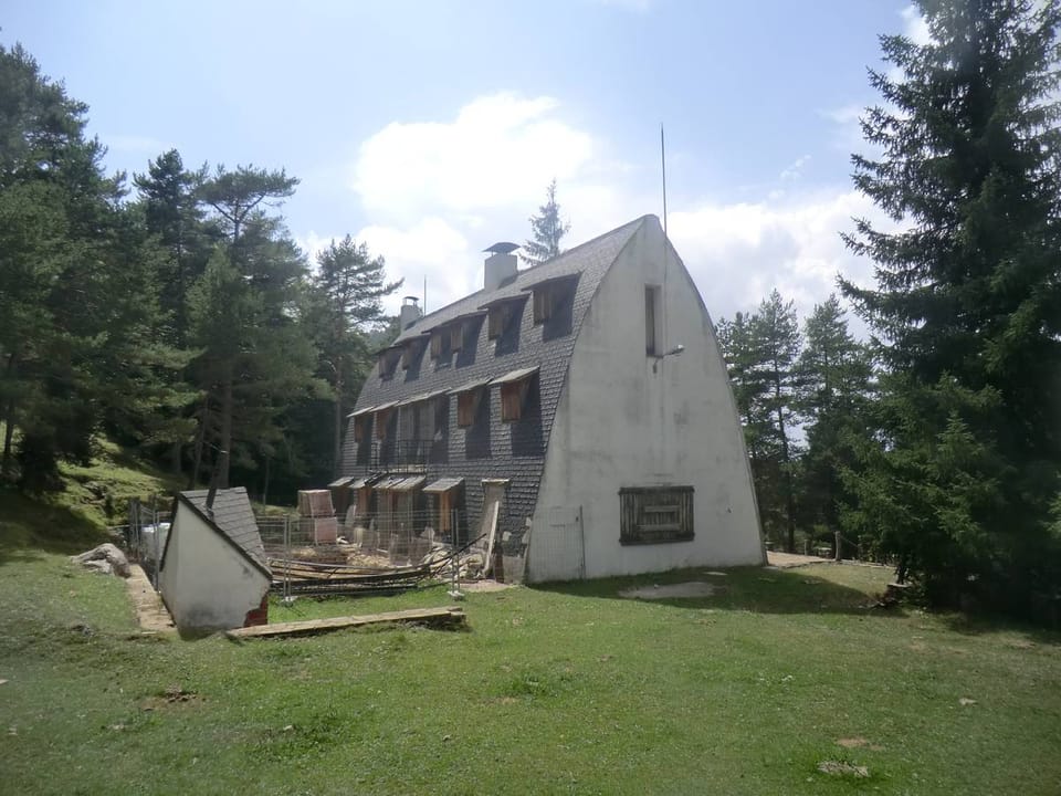 The Xalet del Catllaràs, a stone mountain refuge with a pointed arch roof and an exterior staircase, surrounded by pine trees