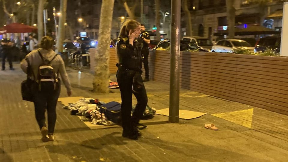 Street vendors quickly setting up makeshift stalls on a busy Barcelona street at night, with police officers in the backgroun