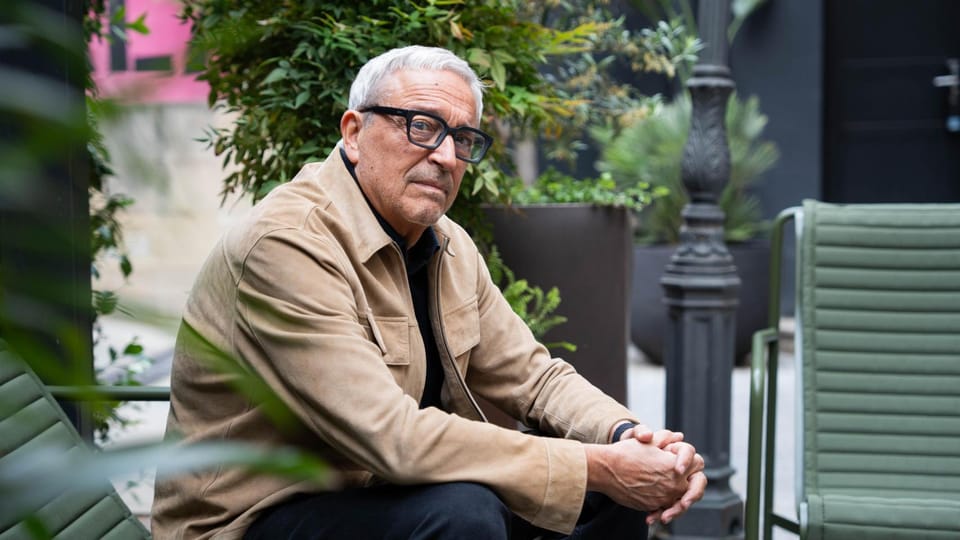 Javier Melero, a man with glasses, speaking at a podium with a book titled "Crímenes decentes" visible.
