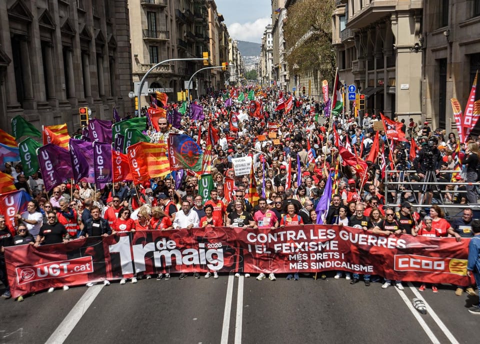 People marching in a May Day demonstration in Barcelona, holding union flags and banners on a city street.