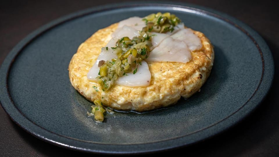 A close-up of a golden, creamy Spanish potato tortilla with a topping, possibly prawn romesco or stewed meat.