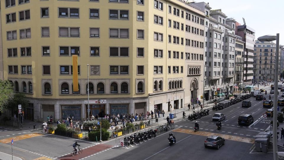 A wide, tree-lined street in Barcelona with expanded pavements and reduced car traffic, showing pedestrians and cyclists enjo
