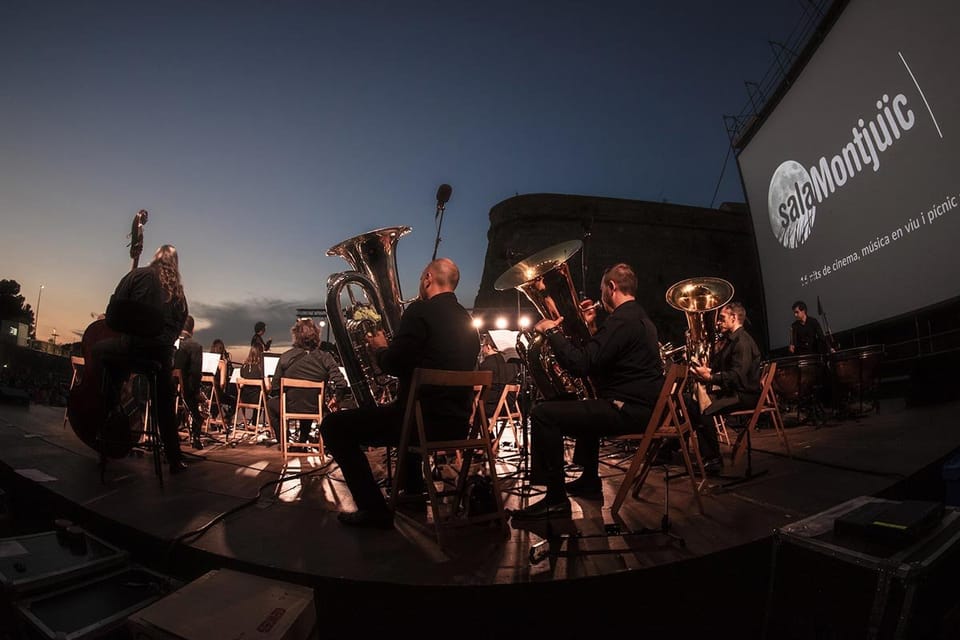 People sitting on a beach at sunset watching a film projected onto a large screen, with the sea in the background.