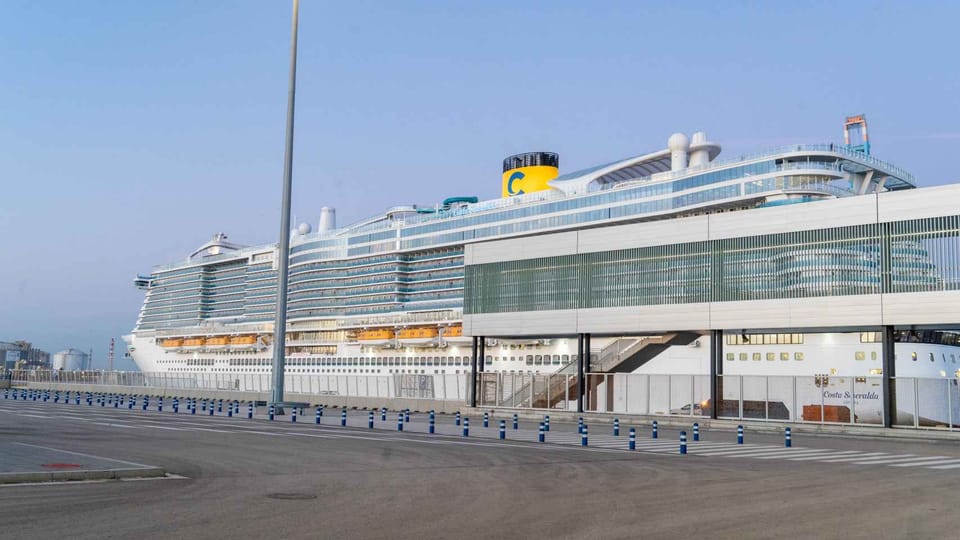 Several large cruise ships docked at the Port of Barcelona with the city skyline in the background under a clear sky.
