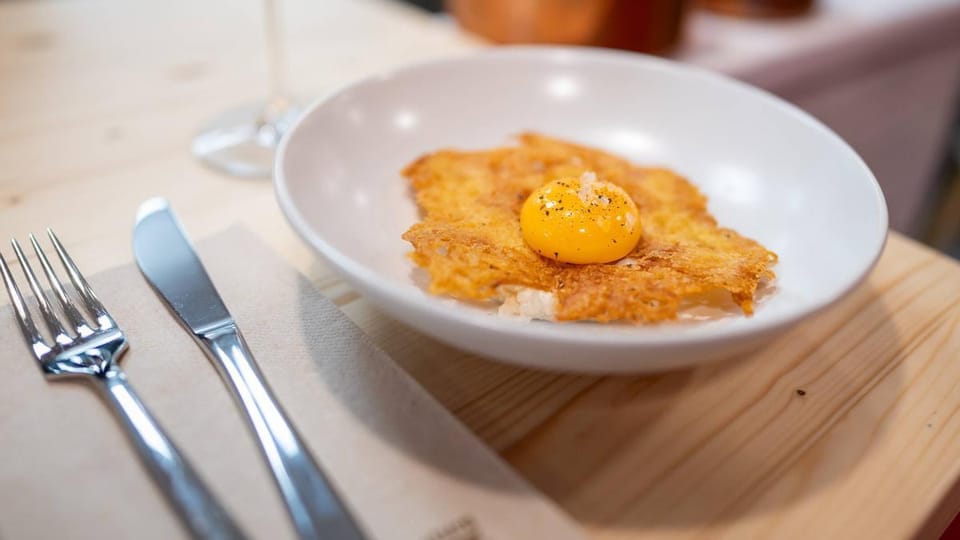 A plate of traditional Catalan 'esmorzar de forquilla' with a fried egg, botifarra sausage, and beans, served in a rustic Bar