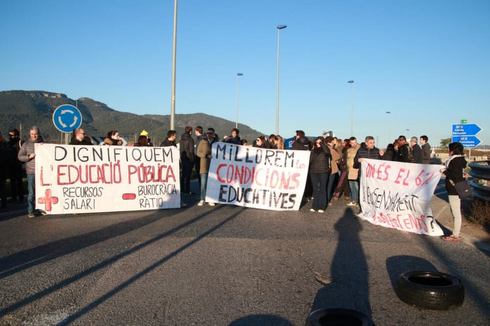 Teachers protesting in Barcelona, holding signs and banners, with police officers in the background.
