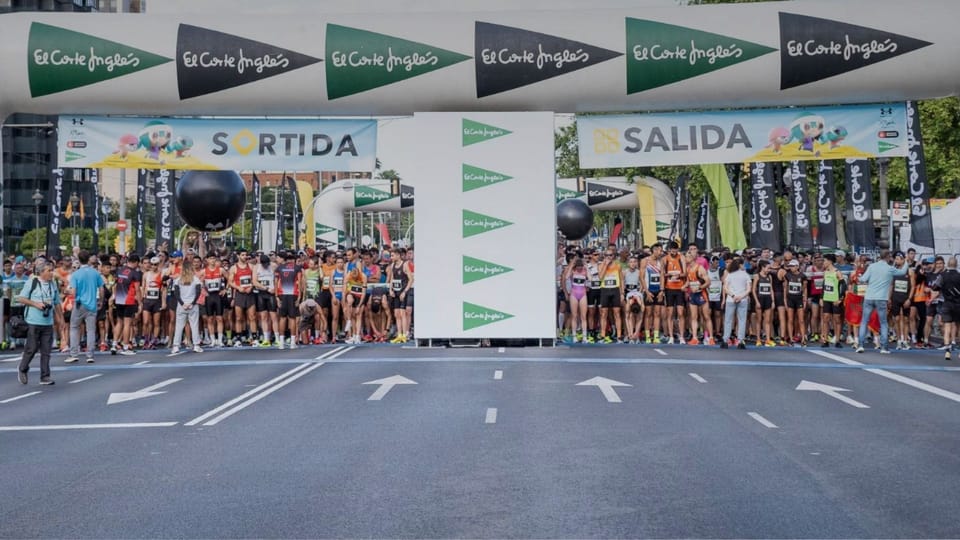 Runners participating in the Cursa El Corte Inglés race in Barcelona, with city buildings in the background.