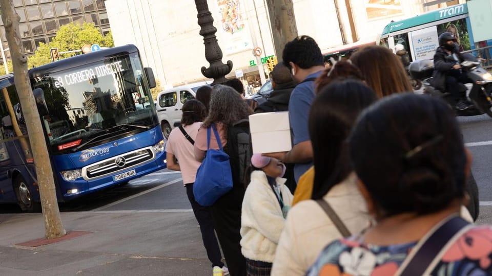 People waiting at a crowded intercity bus stop on Diagonal Avenue in Barcelona, with buses queued behind.