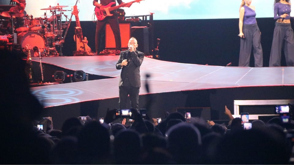Eros Ramazzotti performing live on stage at Palau Sant Jordi, holding a microphone.