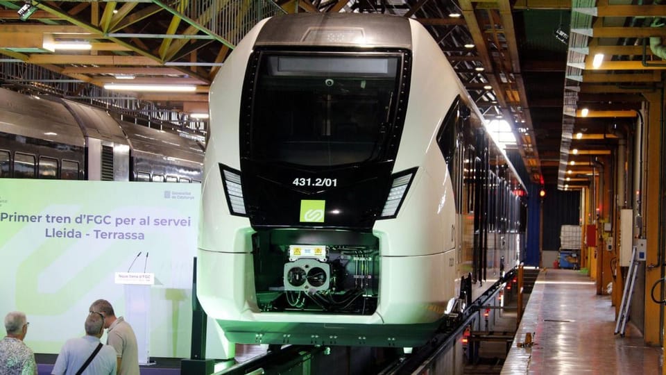 A modern FGC train arriving at a station platform in Catalonia, with passengers waiting.