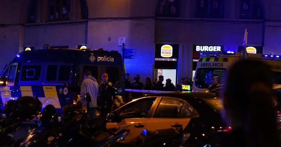 Police tape and emergency services vehicles at a crime scene in a Barcelona street at night.