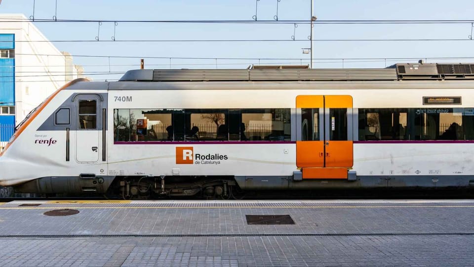 A modern Rodalies train arriving at a station platform in Catalonia, with passengers waiting.