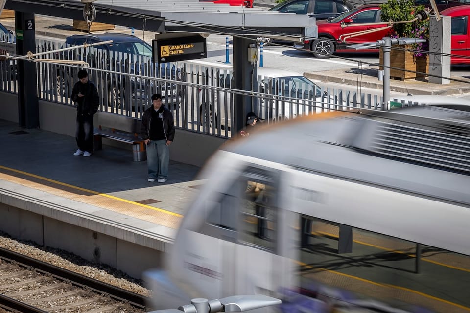 A Rodalies commuter train arriving at a station platform in Barcelona, with passengers waiting to board.