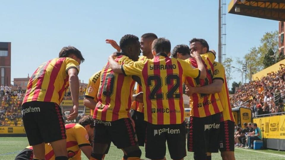 Football players from UE Sant Andreu celebrating a goal or victory on the pitch at Estadi Narcís Sala.