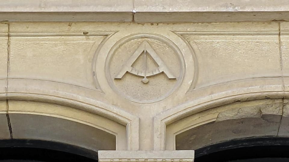 A close-up of a building facade in Sarrià, Barcelona, showing a carved compass and level symbol above a window.