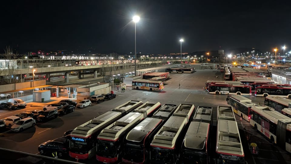 TMB bus being cleaned inside a depot at night, with workers visible.