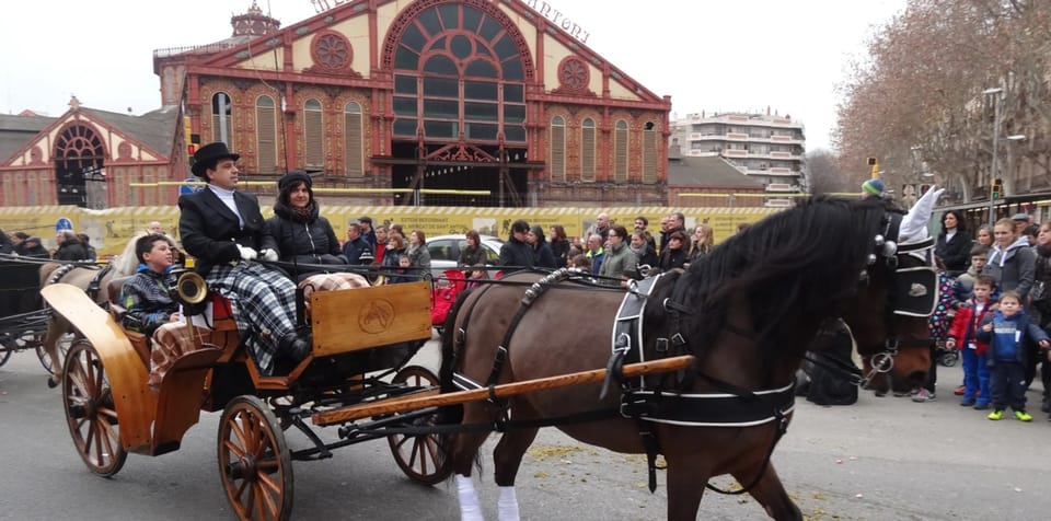 Horses and carriages parading through a city street during the Tres Tombs de Sant Antoni festival in Barcelona.