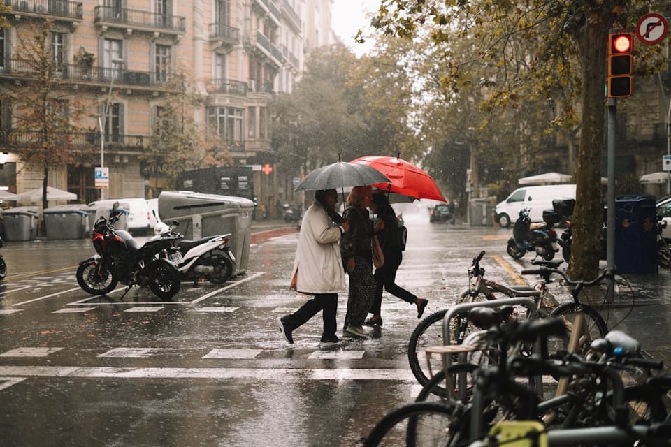 People crossing a Barcelona street with umbrellas in the rain
