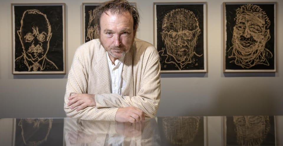 Miquel Barceló, an artist with dishevelled hair, stands in front of his artwork at an exhibition.