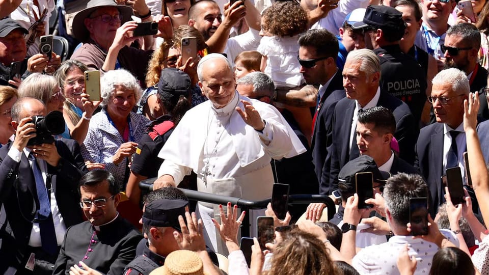 Pope Leo XIV waves from a plane's steps at Barcelona Airport with officials watching his departure.