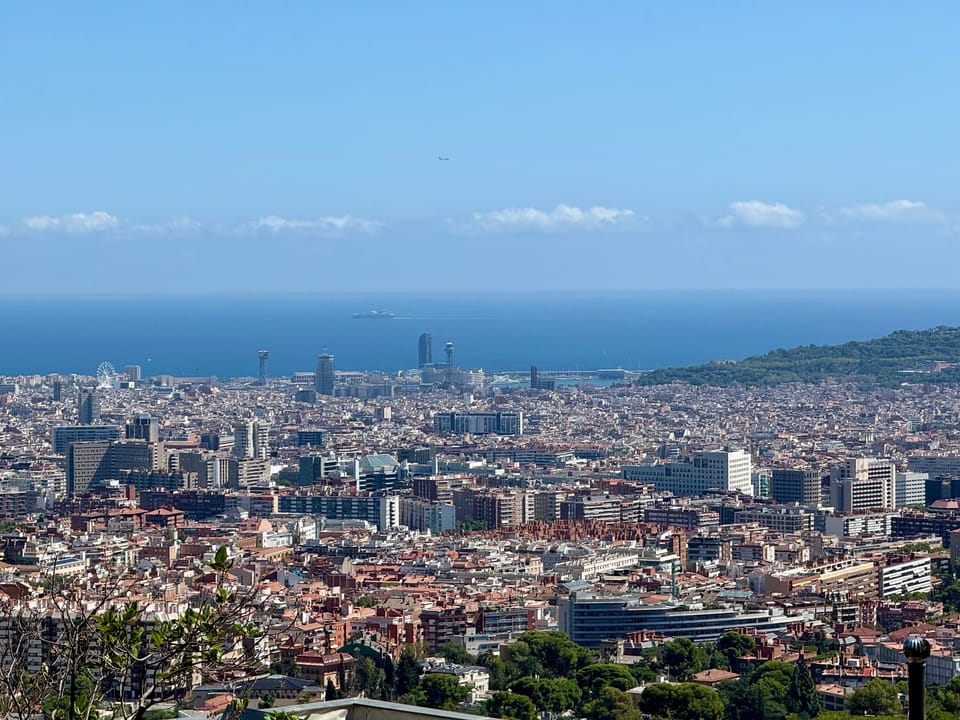 A panoramic view of the Collserola Natural Park bordering Barcelona, with dry summer vegetation and warning signs about forest fire risks visible along a trail.