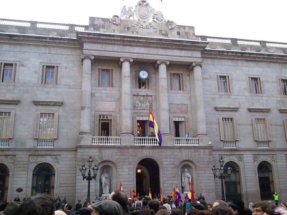 A busy street in central Barcelona with shopfronts, some displaying signs in Catalan, others in Spanish or English only.