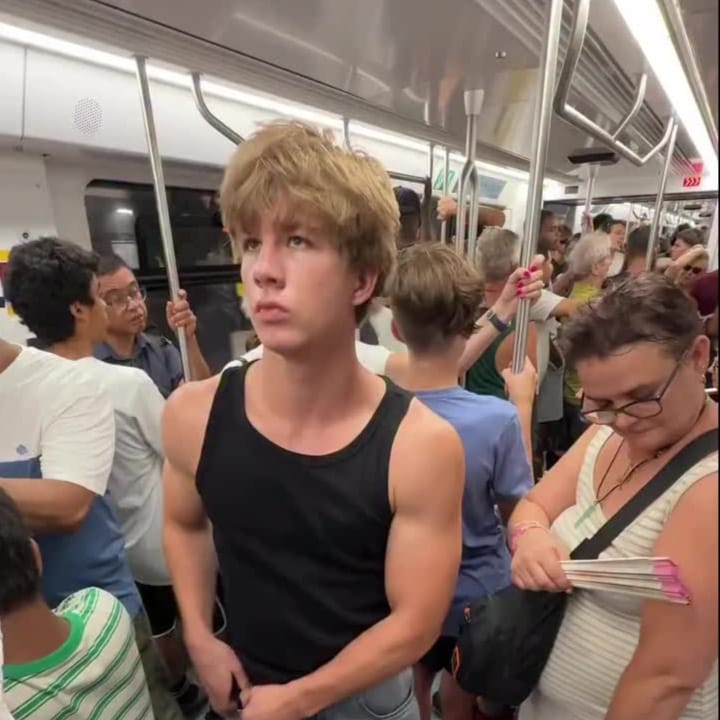 A young man with a wheeled speaker and coloured lights stands in a Barcelona metro carriage, preparing to dance as passengers look on indifferently.