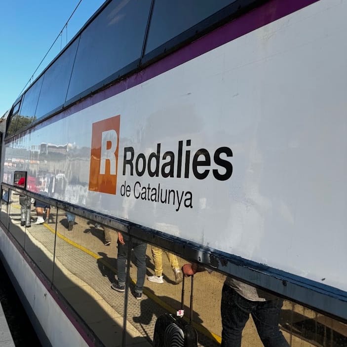 Barcelona Sants station during morning rush hour, with commuters boarding a Rodalies train under digital departure boards.