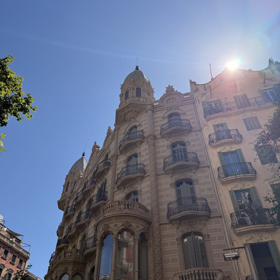 Ornate Modernista apartment facade in Barcelona's Eixample, seen from below against a blue sky