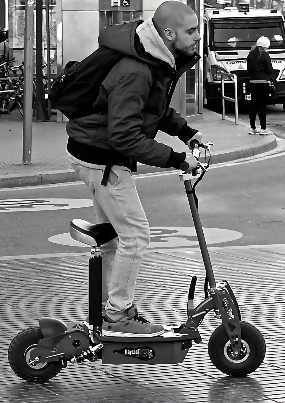 A folded electric scooter standing beside a metro station entrance in Barcelona, with commuters passing by on a weekday morning.