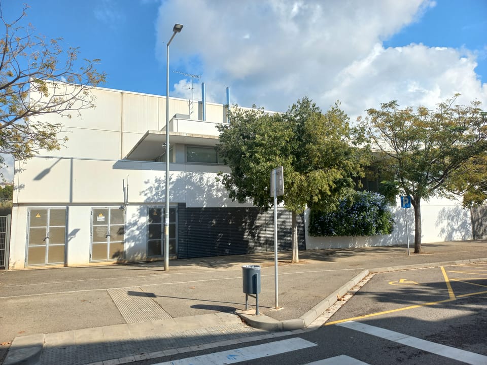 Exterior of a Barcelona public high school on a sunny day, with students outside and city buildings in the background.