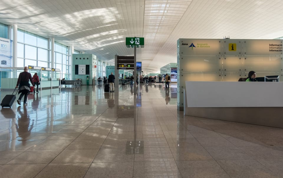 Passengers navigating security at Barcelona-El Prat Airport with information assistants in the background.