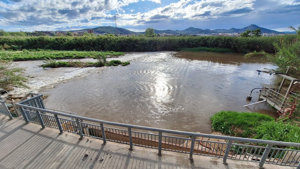 Aerial view of the Llobregat riverfront in Sant Joan Despí showing a tree-lined path alongside the river, with urban areas visible in the background.